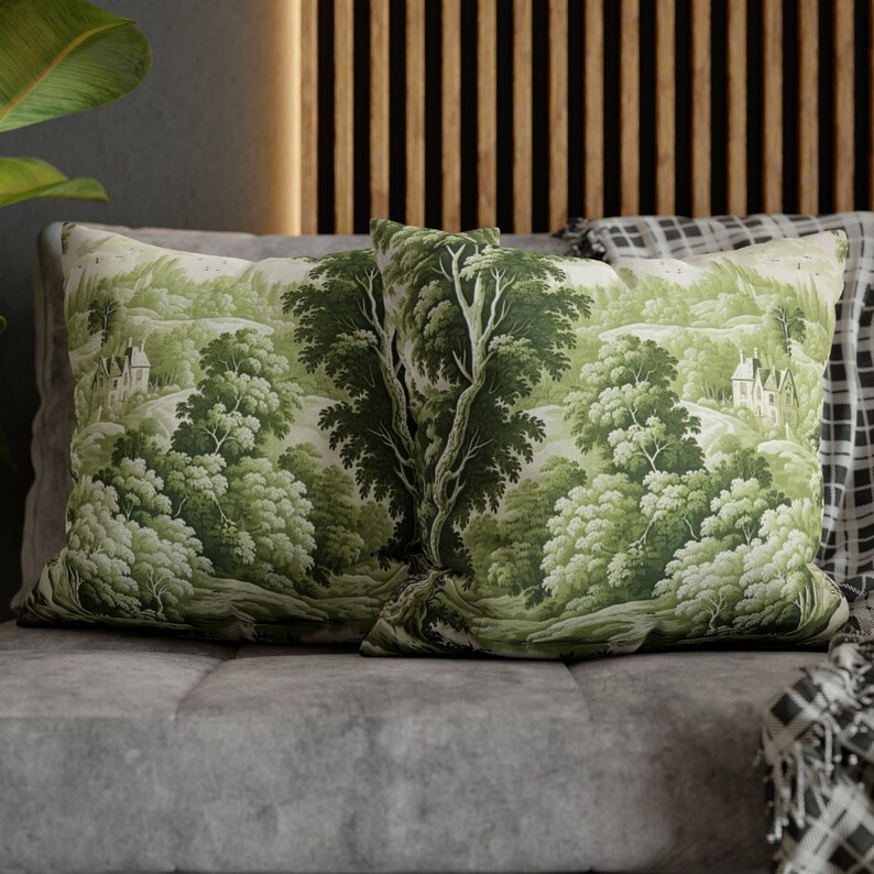 May include: Two green throw pillows with a woodland scene printed on them. The pillows are on a gray couch with a black and white throw blanket.