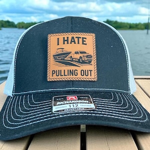 Puede incluir: Gorra de camionero negra y blanca con un parche que dice "I HATE PULLING OUT" encima de una imagen de un barco y una camioneta. La gorra tiene una visera curva y una correa ajustable.
