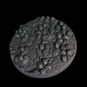 May include: A round, gray, plastic base for miniature figures, featuring a textured surface with a design of numerous skulls.