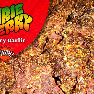 May include: Close-up of spicy garlic jerky. The jerky is dark brown with visible spices and seasonings. A red graphic with the words "IRIE JERKY" and "Spicy Garlic" is in the upper left corner, with the word "FIYAH!" below.