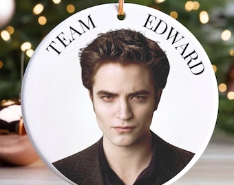 May include: White ceramic Christmas ornament with a portrait of Edward Cullen from the Twilight saga. The ornament has the text "Team Edward" printed on it.