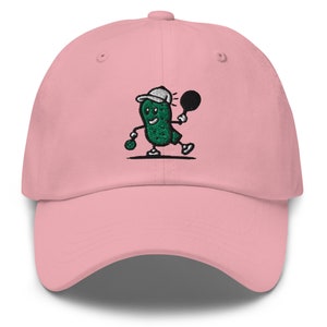 May include: A pink baseball cap with an embroidered green pickle character playing tennis. The pickle is wearing a white hat and holding a tennis racket.