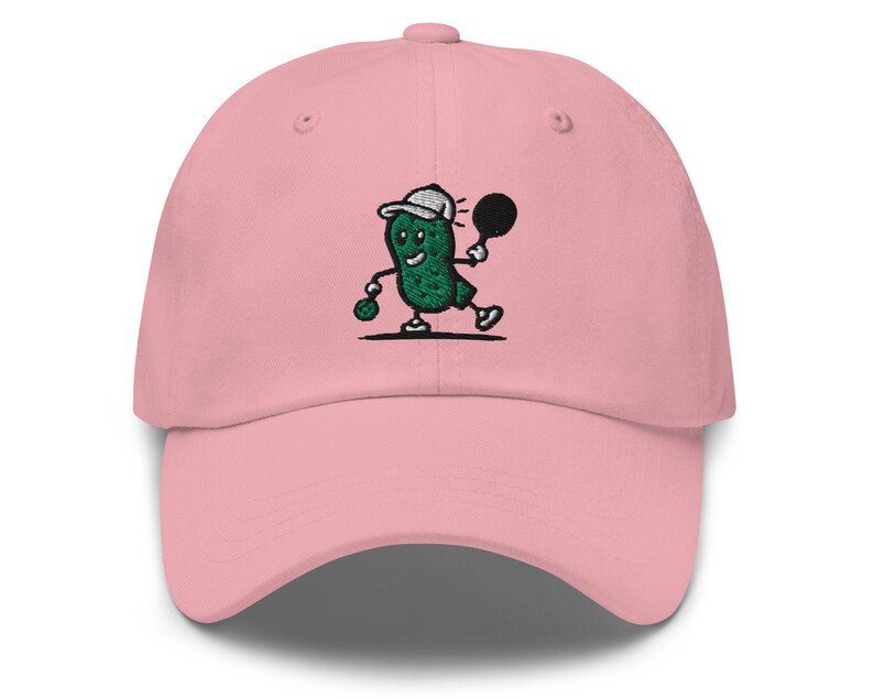 May include: A pink baseball cap with an embroidered green pickle character playing tennis. The pickle is wearing a white hat and holding a tennis racket.