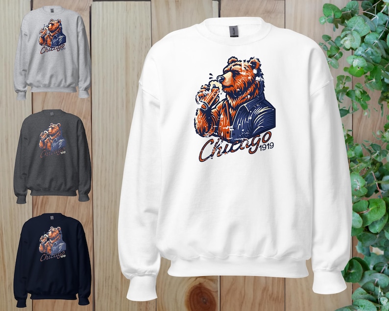 May include: White sweatshirt featuring a graphic of a bear wearing a blue jacket and holding a beer. The bear is looking to the right. The text "Chicago 1919" is below the bear.