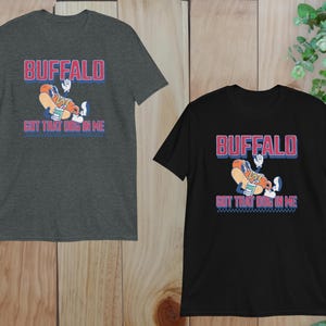 May include: Two short-sleeved t-shirts, one charcoal gray and one black, featuring the text "BUFFALO" in red and blue, with a cartoon hot dog character. The text "GOT THAT DOG IN ME" is below the graphic.