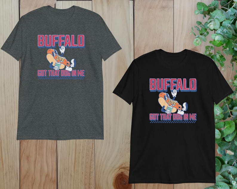 May include: Two short-sleeved t-shirts, one charcoal gray and one black, featuring the text "BUFFALO" in red and blue, with a cartoon hot dog character. The text "GOT THAT DOG IN ME" is below the graphic.