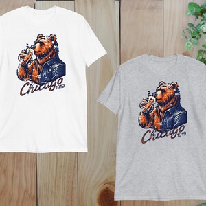 May include: Two t-shirts featuring a graphic of a brown bear wearing a blue jacket and holding a beer. The text "Chicago 1919" is printed on the shirts.