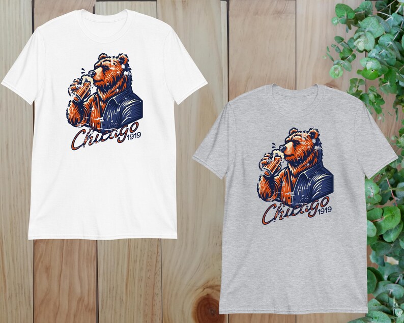 May include: Two t-shirts featuring a graphic of a brown bear wearing a blue jacket and holding a beer. The text "Chicago 1919" is printed on the shirts.