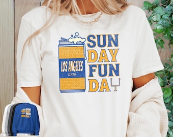 May include: White t-shirt with a graphic design featuring a beer can with the text "LOS ANGELES 1936" and the words "SUNDAY FUN DAY" in blue and yellow. A football goalpost is also included.