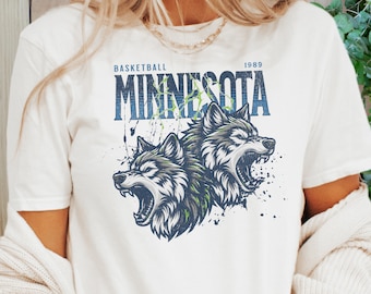 May include: White t-shirt with a graphic print of two wolves with their mouths open, the text "Basketball Minnesota 1989" is printed above the wolves.