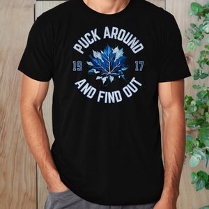 May include: Black t-shirt with a blue and white maple leaf graphic and the text "Puck Around 19 17 And Find Out".