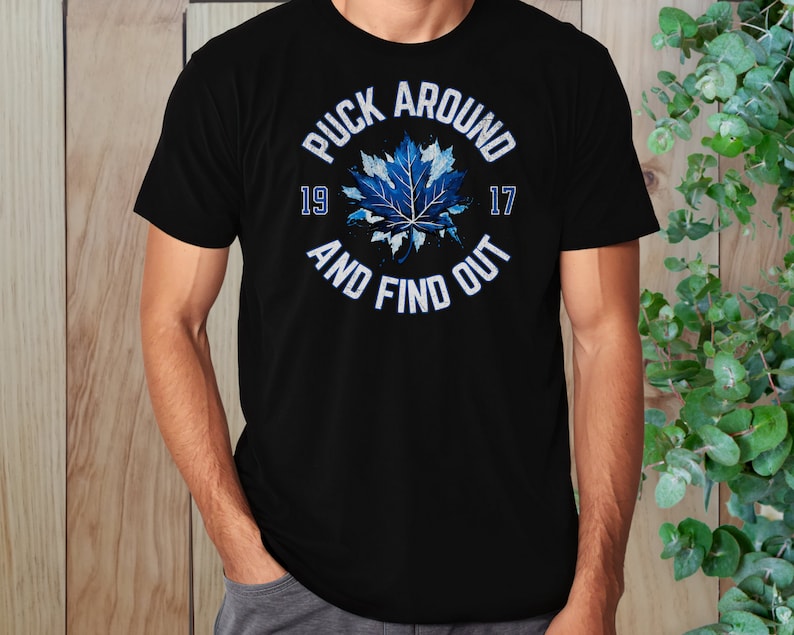 May include: Black t-shirt with a blue and white maple leaf graphic and the text "Puck Around 19 17 And Find Out".