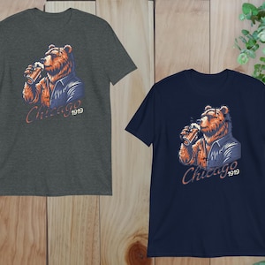 May include: Two t-shirts featuring a graphic of a brown bear wearing a blue jacket and holding a beer. The text "Chicago 1919" is printed on the shirts.