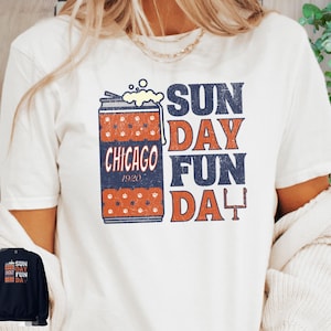 May include: Cream-colored t-shirt featuring a graphic design with a beer can illustration and the text "SUN DAY FUN DAY CHICAGO 1920". The design includes orange and navy blue elements. Several other shirt colors are shown below.