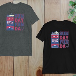 May include: Two t-shirts with a graphic of a can of Buffalo beer with the text "Sunday Fun Day" printed on them. The shirt on the left is dark gray and the shirt on the right is black.