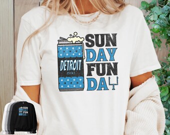 May include: White t-shirt featuring a Detroit-themed design. The graphic includes a blue and black beer can with the text "DETROIT 1930" and the words "SUNDAY FUN DAY" in blue and black. A small image of the shirt is shown in the bottom left corner.