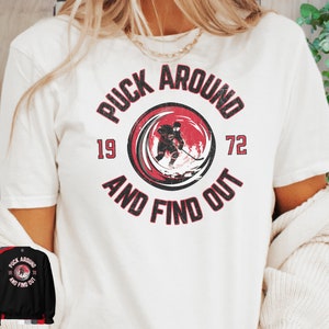 May include: White t-shirt with a red and black graphic that says "Puck Around and Find Out" with a hockey player in the center. The numbers 19 and 72 are on either side of the graphic.