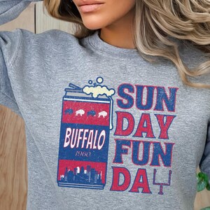 May include: Gray sweatshirt with a vintage-style graphic of a can of beer with the text "Buffalo 1960" and the words "Sun Day Fun Da" in red and blue.