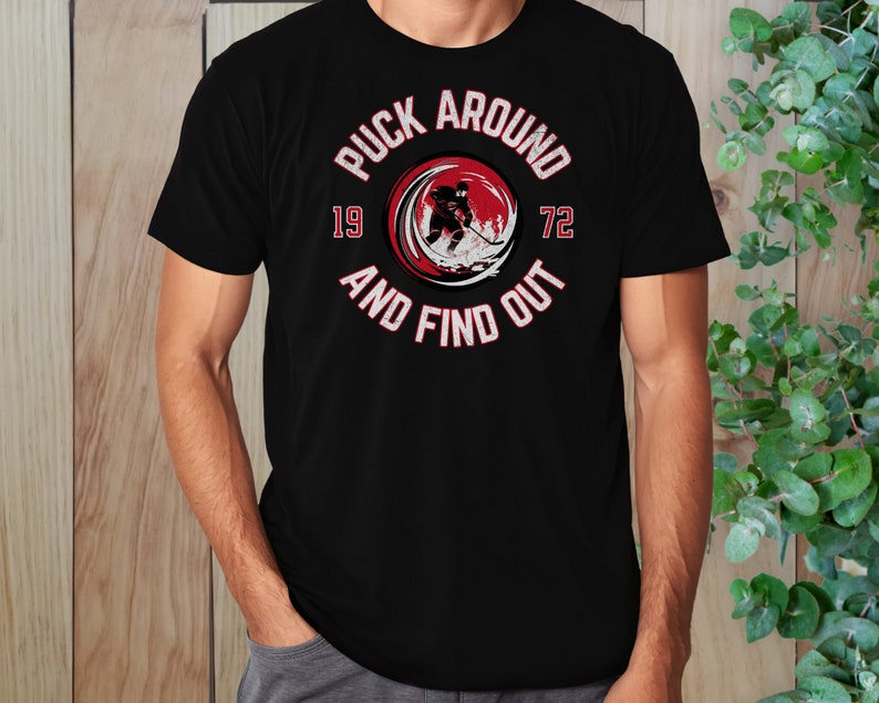 May include: Black t-shirt with a red circle graphic featuring a hockey player and the text "Puck Around 19 72 And Find Out".