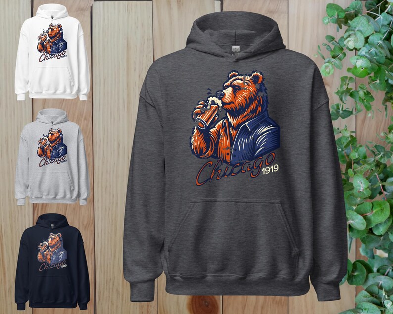 May include: A dark grey hooded sweatshirt featuring a cartoon illustration of a bear wearing a blue jacket and holding a beer. The bear is looking to the right and the text "Chicago 1919" is printed below the bear.