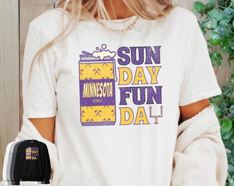Può includere: Maglietta bianca con una grafica viola e gialla di una lattina di birra con il testo "Minnesota 1961" e il testo "Sun Day Fun Day" con un palo della porta da calcio.