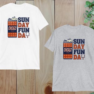 May include: Two short-sleeved t-shirts, one white and one gray, featuring a graphic design. The design includes a can with the text "Chicago", "Sunday Fun Day", and a football goalpost. The shirts are made of a soft material.