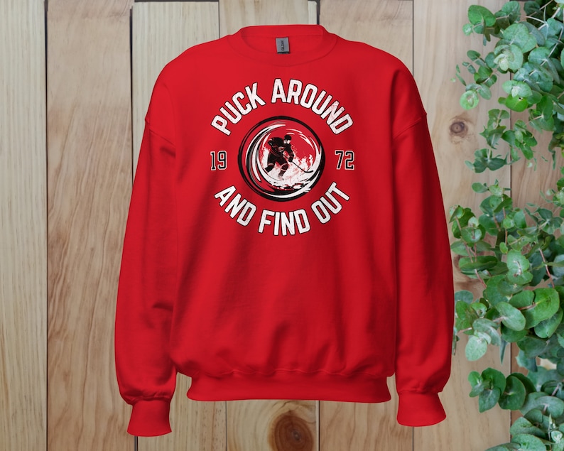 May include: Red sweatshirt with a white graphic of a hockey player in a circle with the text "Puck Around 19 72 And Find Out".