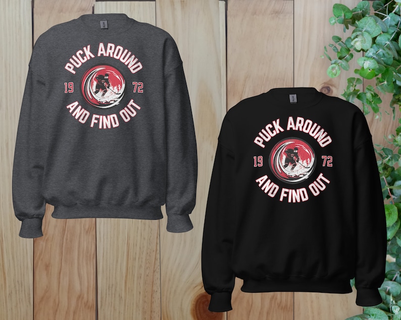 May include: Two sweatshirts with a hockey player graphic and the text "Puck Around 19 72 And Find Out". One sweatshirt is black and the other is dark gray.