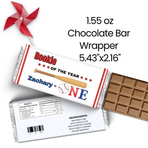 May include: A white chocolate bar wrapper with red and blue accents. The wrapper features a baseball bat and ball, the text "Rookie of the Year", and the name "Zachary is One". The wrapper is 13.8 cm by 5.5 cm and is for a 44 g chocolate bar.