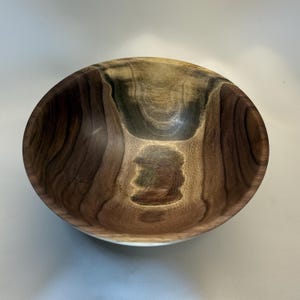 May include: A handcrafted wooden bowl with a natural, organic design. The bowl features a blend of light and dark brown tones, showcasing the wood grain. The interior has a smooth finish, perfect for serving or display.