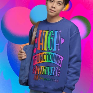 Puede incluir: Una sudadera azul marino con un gráfico de arcoíris que dice "HIGH FUNCTIONING INTROVERT still leave me alone".
