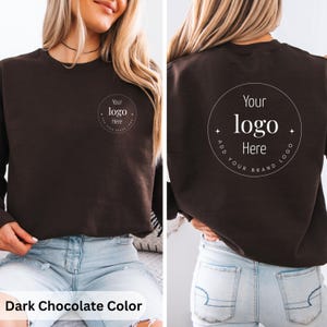 May include: Dark chocolate-colored sweatshirt with a crew neck. The front features a circular logo design with the text "Your logo Here". The back of the sweatshirt also displays the same logo design. The text "Add Your Brand Logo" is included in the design.
