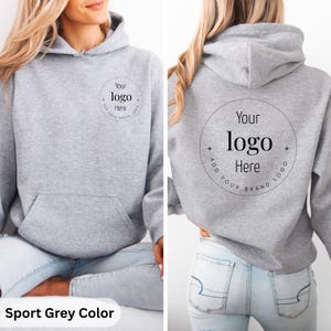May include: Sport grey hoodie with a front kangaroo pocket and a hood. The front and back of the hoodie feature a circular design with the text "Your logo Here" in a black font. The bottom of the image has the text "Sport Grey Color".