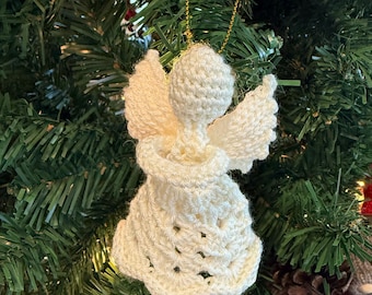 May include: A white crocheted angel ornament hanging on a green Christmas tree. The angel has a white dress and wings.