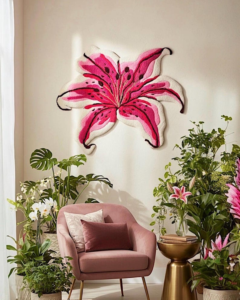May include: A large, wall-mounted tufted textile art piece shaped like a blooming lily flower. The petals are rendered in shades of vibrant magenta, soft pink, and cream, featuring dark purple spots and defined black outlines along the edges.