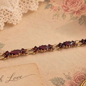 Può includere: Un bracciale in metallo color oro caratterizzato da una serie di pietre rosso scuro, taglio marquise, montate su griffe. Il bracciale è composto da maglie ripetute che alternano le pietre marquise più grandi a pietre rosse rotonde.