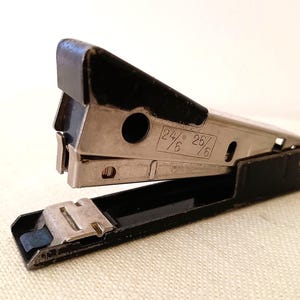 May include: A vintage stapler in black and silver. The stapler features a black handle and base, with a silver metal body. The text "24/6" and "25/6" is printed on the side. A classic office supply for home or workplace.