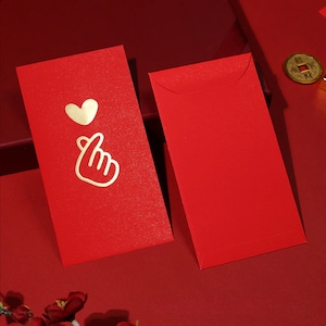 May include: Two red envelopes with gold accents. One envelope has a gold heart and a gold hand making a heart shape. The other envelope is plain.