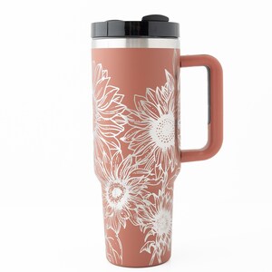 May include: A terracotta-colored stainless steel travel mug with a black lid and a handle. The mug features a white floral design of sunflowers.
