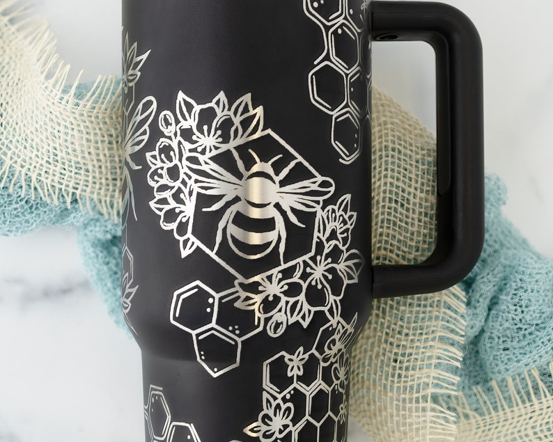Stanley brand 40 oz tumbler in black with bumble bee and honeycomb design wrapped around the tumbler. Close up on bumble bee.