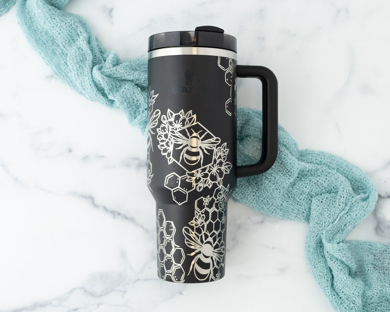 Stanley brand 40 oz tumbler in black with bumble bee and honeycomb design wrapped around the tumbler. Front view.