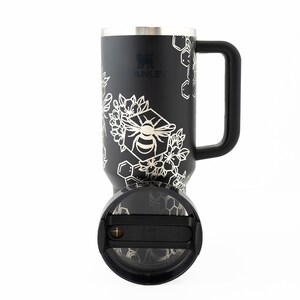 Stanley brand 40 oz tumbler in black with bumble bee and honeycomb design wrapped around the tumbler. Shown with lid facing front.