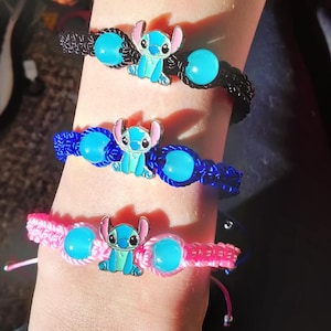 May include: Three handmade bracelets in black, blue, and pink. Each bracelet features a cartoon character charm and turquoise-colored beads. The bracelets are made of woven cord and are adjustable.