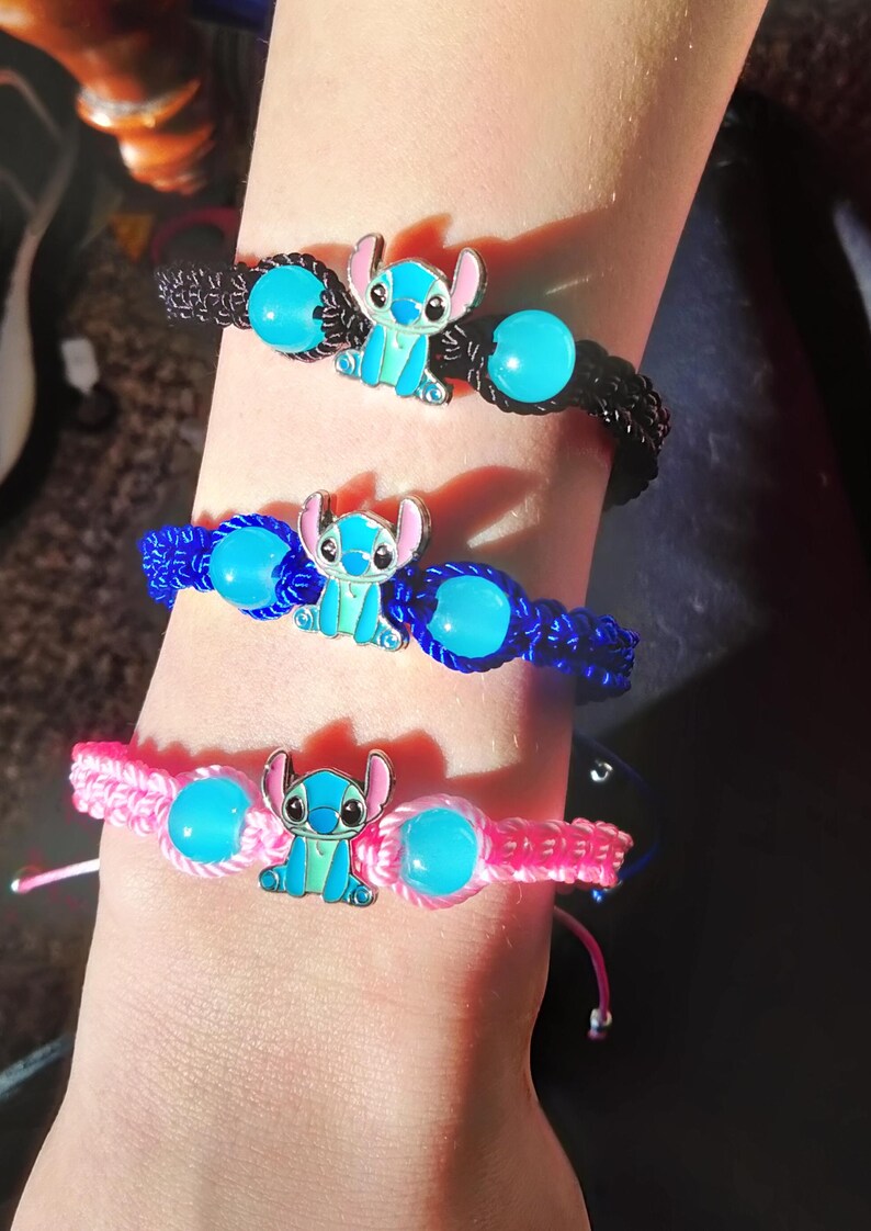 May include: Three handmade bracelets in black, blue, and pink. Each bracelet features a cartoon character charm and turquoise-colored beads. The bracelets are made of woven cord and are adjustable.