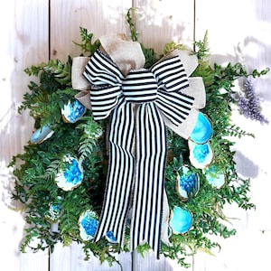 May include: A wreath made of green foliage with blue and white oyster shells and a black and white striped bow.