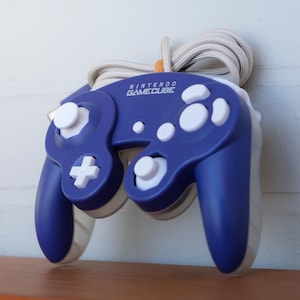 May include: A blue Nintendo GameCube controller with white buttons and a white cord. The controller has a white faceplate with the words "Nintendo GameCube" printed on it.