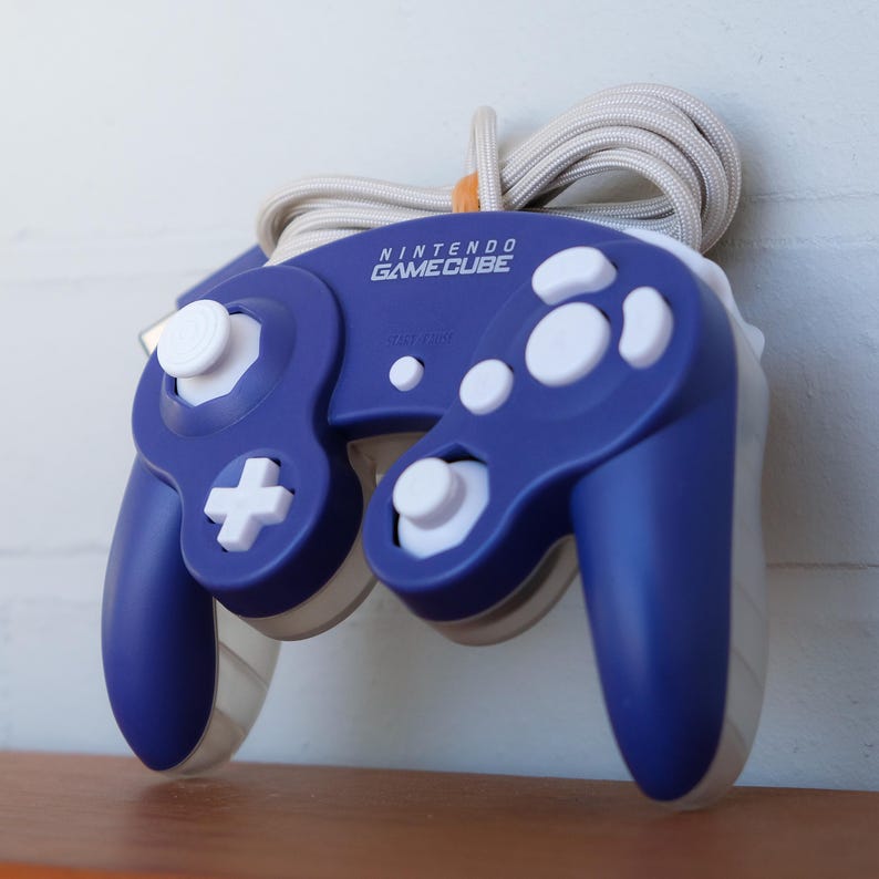 May include: A blue Nintendo GameCube controller with white buttons and a white cord. The controller has a white faceplate with the words "Nintendo GameCube" printed on it.