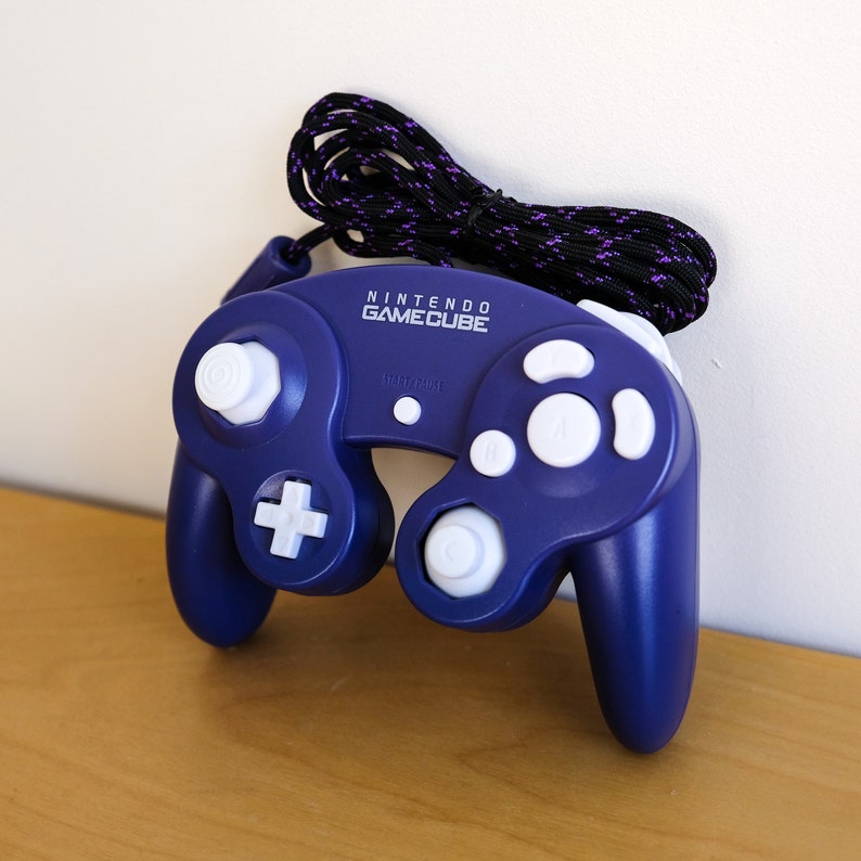 May include: A blue Nintendo GameCube controller with white buttons and a black and purple cord.
