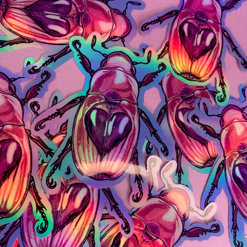 May include: A collection of iridescent beetle stickers with a holographic finish. The beetles are pink, purple, and blue with a heart-shaped design on their backs.