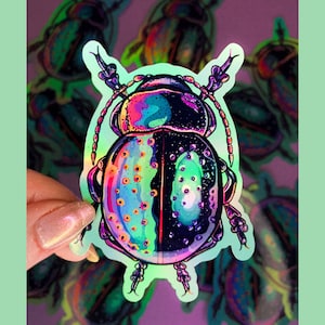May include: A holographic sticker of a beetle with iridescent green, blue, and purple colours. The beetle has a black body with white dots and is surrounded by a light green background.